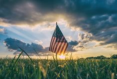 an american flag is in the middle of a grassy field as the sun goes down