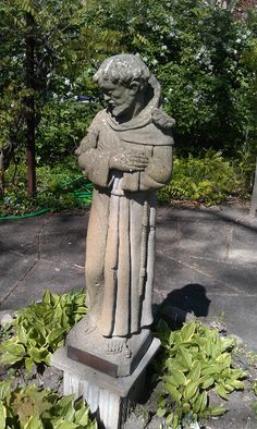 a statue of a man holding a book in his hands and standing next to some bushes