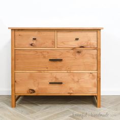 a wooden dresser sitting on top of a hard wood floor next to a white wall