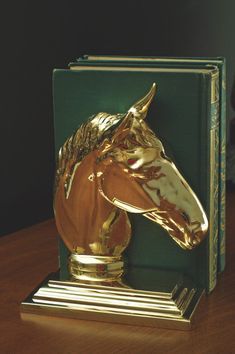 a golden horse head is on top of a green book holder with gold trimmings