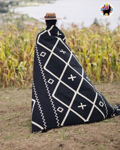 a person wrapped in a blanket sitting on the ground next to cornfield with a lake behind them