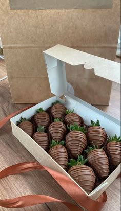 a box filled with chocolate covered strawberries on top of a wooden table next to a ribbon