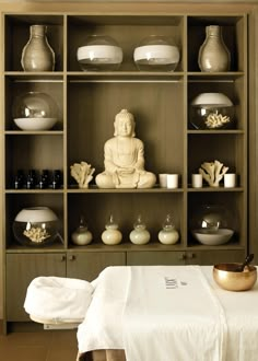 a buddha statue sitting on top of a wooden shelf filled with bowls and plates next to a white bed