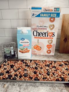 a box of cheerios next to a baking pan with cereal and milk on it