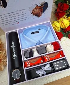 an open gift box containing sunglasses, tie and other personal items with flowers in the background