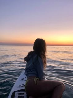 a woman sitting on the back of a surfboard in the ocean at sunset or dawn