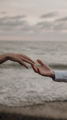 two people reaching out their hands to touch each other on the beach near the ocean