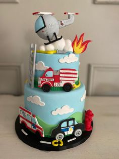 a birthday cake with an airplane, firetruck and truck on the top tier