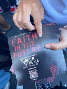 a person pointing to a ticket for a concert with the words faith in the future written on it