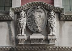 two lion statues on the side of a building with a coat of arms above it