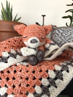 an orange and white crocheted blanket with a small stuffed animal on top of it