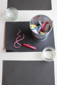 some crayons are sitting in a bucket on top of a black paper with pink writing