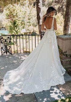 a woman in a wedding dress looking at the back of her gown, with trees and bushes behind her