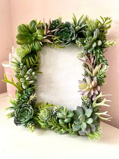 a square frame made out of succulents on a white countertop next to a potted plant