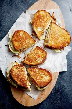 four grilled sandwiches cut in half on top of a wooden board with wax paper