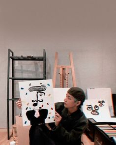 a woman sitting on the floor holding up a painting