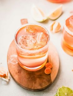 two glasses filled with drinks sitting on top of a wooden plate next to sliced oranges