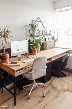 a desk with two computers and plants on it