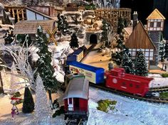 a model train set up in the snow with trees and houses on it's sides