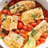 some fish and tomatoes are in a white bowl with lemon wedges on the side