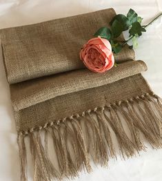 a pink rose sitting on top of a burlocked table cloth with tassels