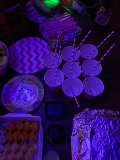 a table topped with plates and cups filled with food next to purple lite candles