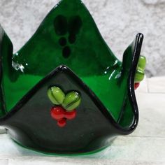 a green and black glass vase with red berries on the bottom is sitting on a white surface