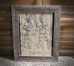 a framed drawing of two people holding hands in front of a wooden frame on top of a table