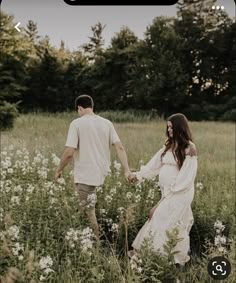 a man and woman holding hands while walking through a field with wildflowers in the foreground