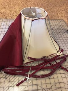 a lamp shade with scissors on top of it next to a piece of red cloth