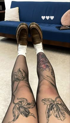 the legs and ankles of a woman with tattoos on her body, sitting in front of a blue couch