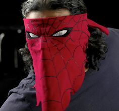 a man wearing a red spiderman mask with his face covered by black hair and grey eyes