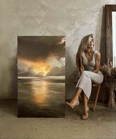 a woman sitting on a chair in front of an art piece with the sun setting