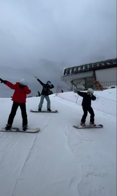 three snowboarders are standing in the snow with their arms up and one is on his board