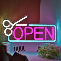 a neon sign that says open with scissors and a bowl of flowers next to it