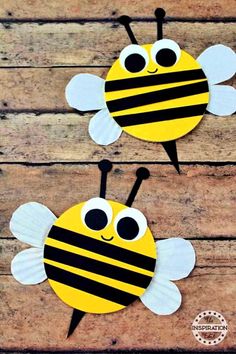 two bees made out of paper sitting on top of a wooden table