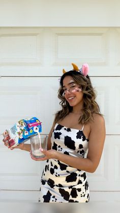 a woman in a cow print dress holding a drink and candy bar with horns on her head