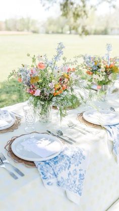 a table set with plates, silverware and vases filled with flowers on it