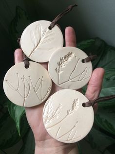 four ceramic discs with leaves on them are being held by a person's hand