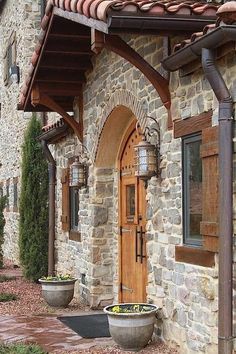 a stone house with two large planters on the front porch and an arched wooden door