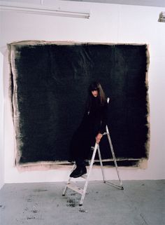 a woman is sitting on a ladder in front of a blackboard that has been painted