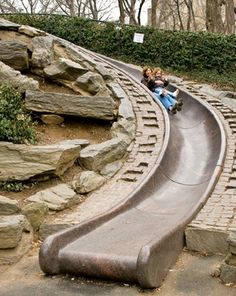 two children are riding on a slide in the park