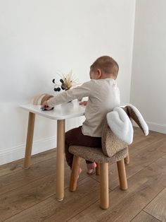 a small child sitting at a table with a stuffed animal on it's back