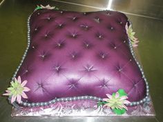 a purple cake sitting on top of a metal counter covered in frosting and flowers