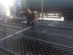 two men are working on a large metal cage in a warehouse or yard, one is looking down at the ground