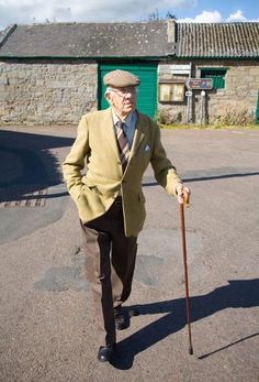 an old man in a suit and hat walking with a cane