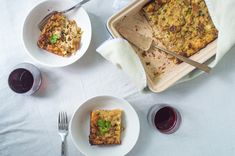 two white plates with food on them next to some wine glasses and utensils