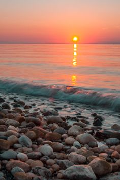 the sun is setting over the ocean with rocks