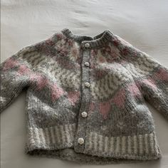 a knitted cardigan with pink and grey designs on the front, sitting on a white surface