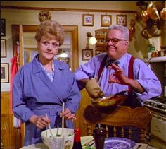 an older man and woman in the kitchen preparing food for their dinner table with utensils